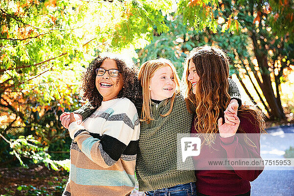 Three pretty tween girls laughing together outdoors in fall colors.