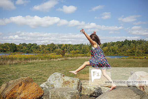a little barefoot child leaps across large boulders outside