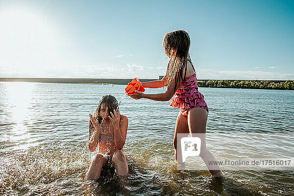 Young girl splashing big sister with water in lake