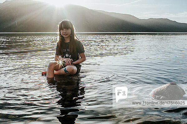 Young girl sitting on a rock in a lake on a sunny day