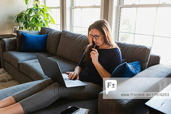 Woman sitting on sofa in living room working on computer.
