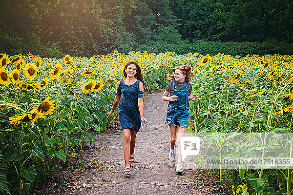 Two happy tween girls running in a sunflower field.