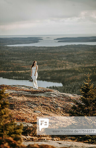 Bride in wedding gown with bouquet on mountain in Maine