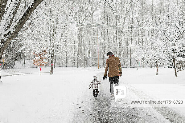 Dad and toddler walk down street on a snowy day in a neighborhood