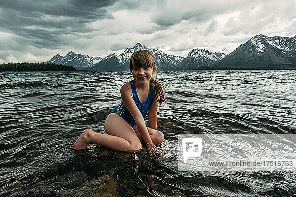 Young girl sitting on a rock in a mountain lake