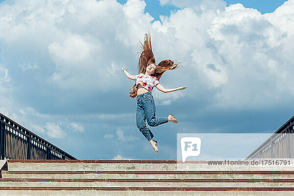Young teen girl jumping up on the blue cloudy sky background