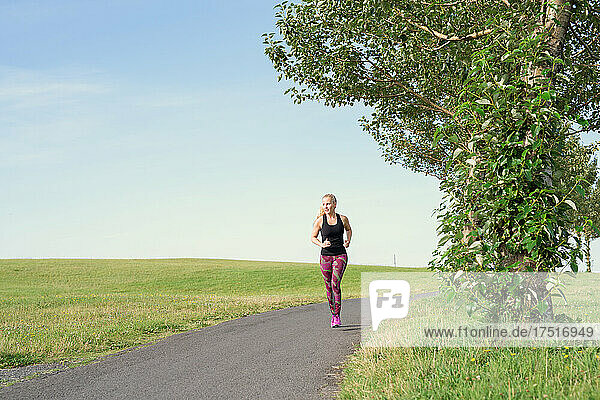 Fit blondie running on path in countryside against cloudless blue sky