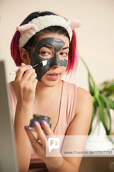Woman with pink hair inflicts face mask of therapeutic clay.