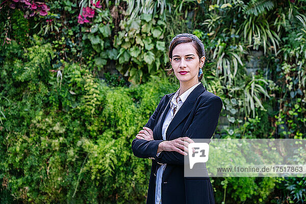 Elegant young businesswoman looking at camera while standing in park