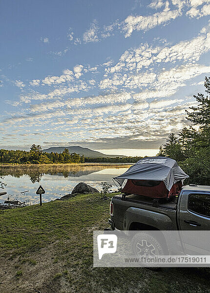 Truck with tent sits next to peaceful river with mountain  Maine