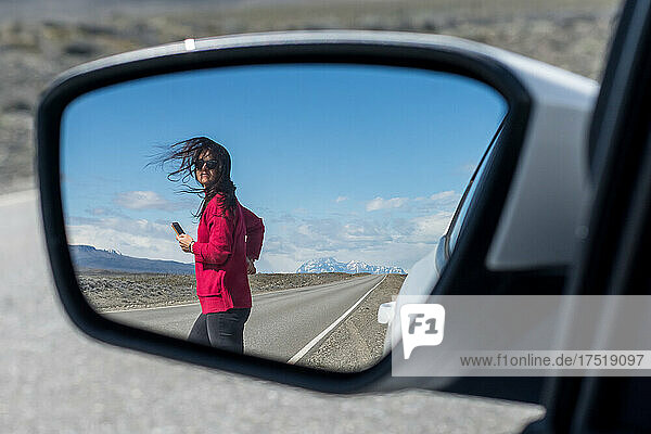 Woman crossing the route seen through side-view mirror of car