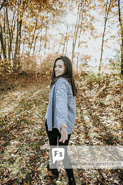 smiling young woman walking through woods in fall looking at camera
