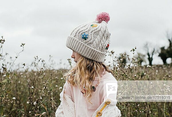 portrait of a young girl with flowery hat on stood in a flowery field