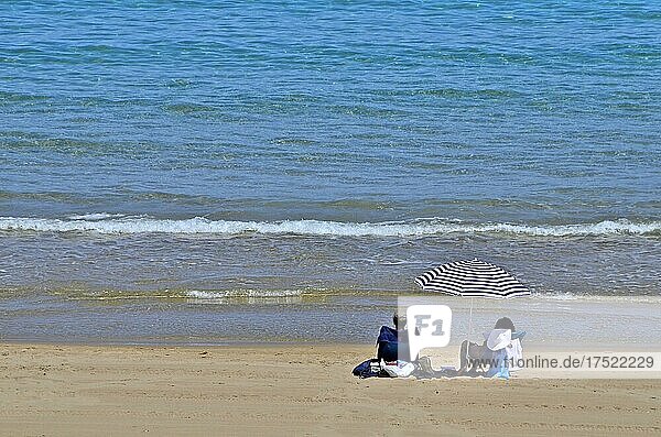 Mann und Frau unter Sonnenschirm vor Welle am Strand  Quatro Calas  Hospitalet dEnfant  Katalonien  Spanien  Europa