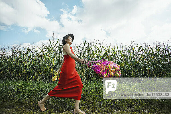Carefree woman with mesh bag walking on corn field