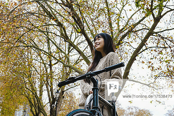 Lächelnde Frau lehnt auf Fahrrad unter Baum