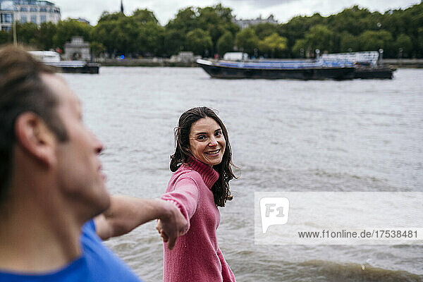 Smiling woman holding hands of man at riverbank