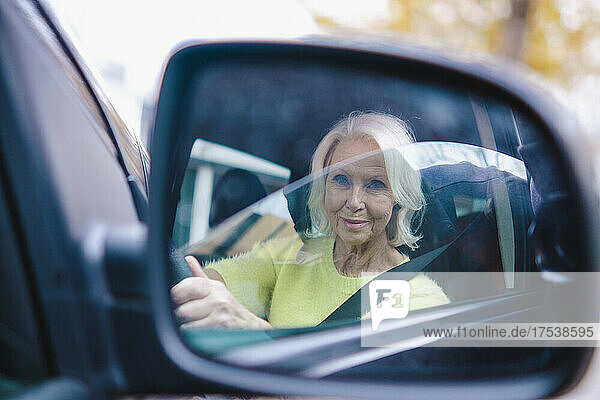 Rentnerin fährt Auto und reflektiert im Seitenspiegel