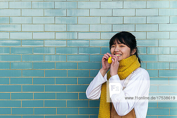 Smiling woman holding balloon in front of brick wall