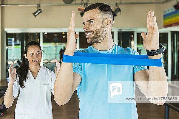 Sportsman listening to fitness instructor guiding from behind at gym