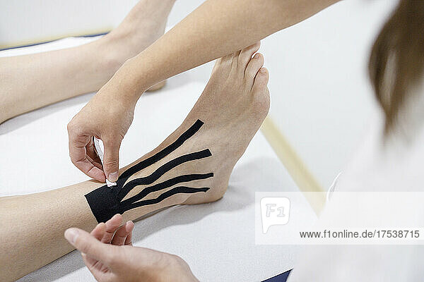 Physical therapist applying therapeutic tape on athlete's leg at massage table