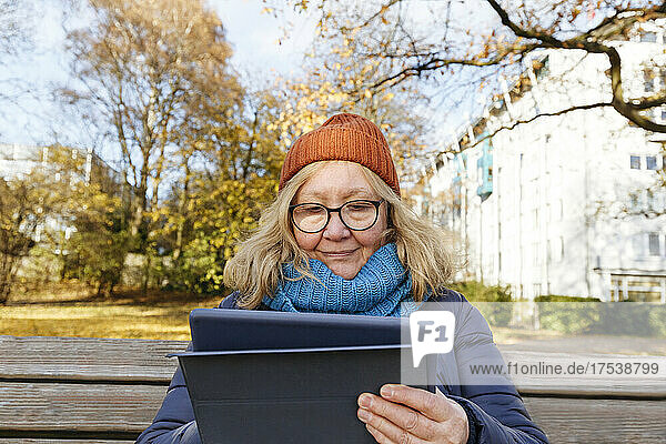 Senior woman using tablet PC sitting on bench in park