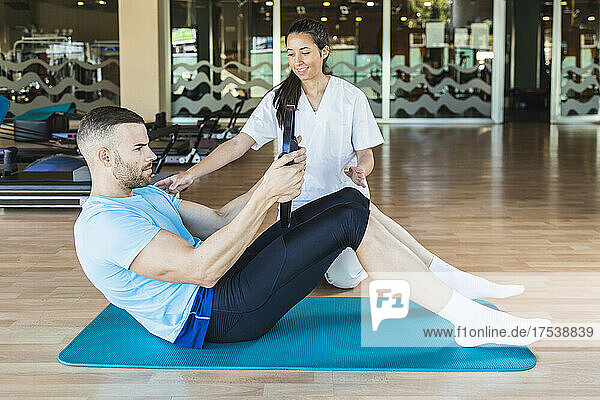 Fitness instructor helping sportsman doing pilates exercise in gym