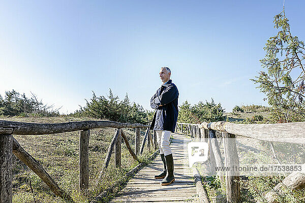 Man standing with arms crossed on wooden bridge