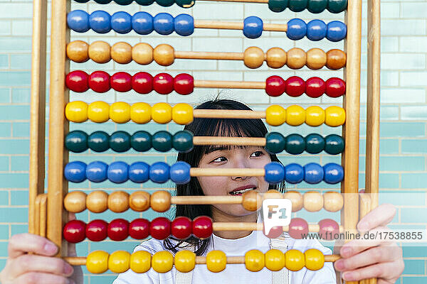Thoughtful woman with multi colored abacus in front of brick wall