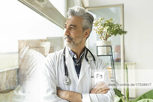 Thoughtful doctor with arms crossed looking out through window