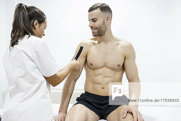 Sportsman looking at physical therapist applying therapeutic tape