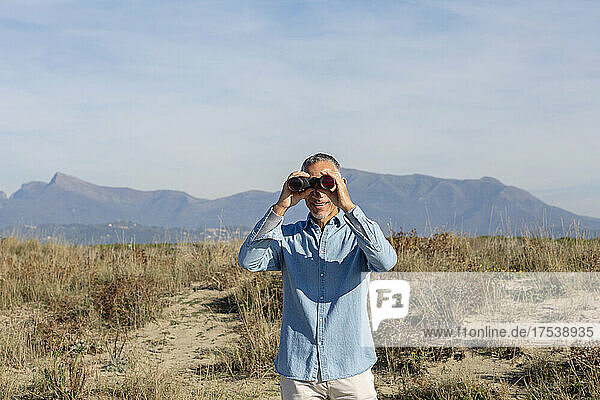 Mann schaut durch ein Fernglas und steht in der Wüste