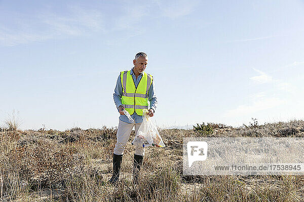 Mann sammelt Plastikflaschen aus Sanddünen ein