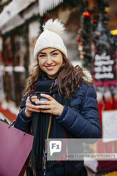 Young woman wearing knit hat enjoying mulled wine at Christmas Market