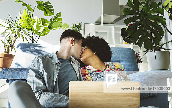 Young couple kissing on mouth with laptop in living room