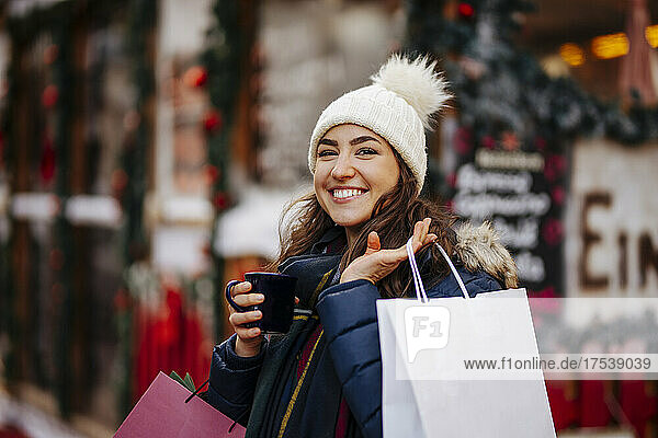 Lächelnde Frau mit Einkaufstüten und Wein genießend