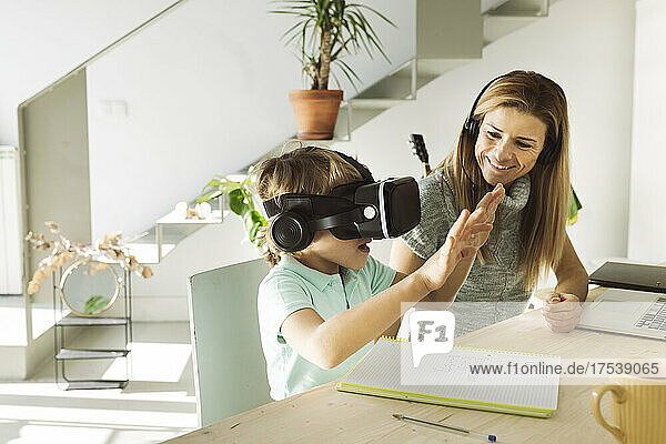 Happy woman looking at son wearing virtual reality simulator at home