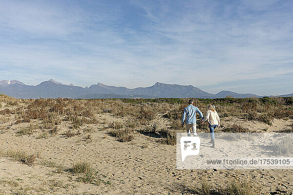 Couple walking together amidst plants on sand at dunes