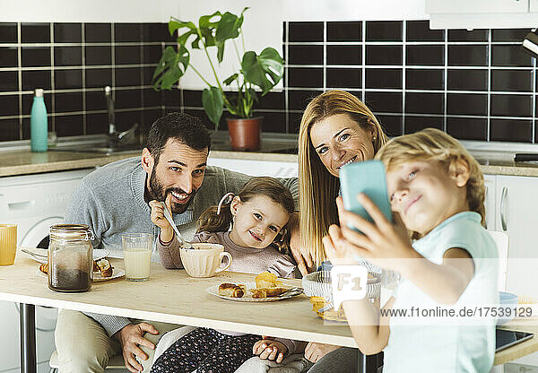 Boy taking selfie with happy family at breakfast table