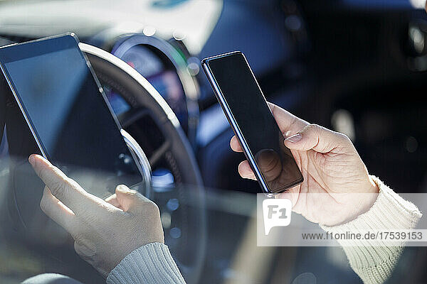 Man's hands holding mobile phone and tablet PC inside car
