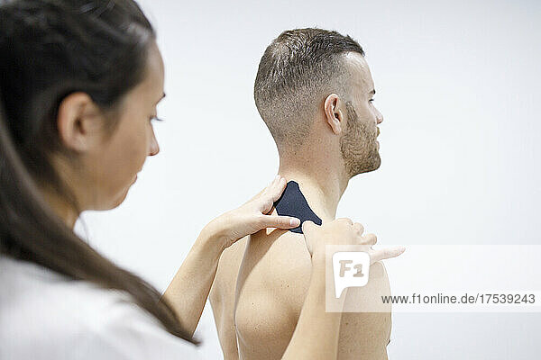 Physical therapist putting therapeutic tape on athlete's shoulder