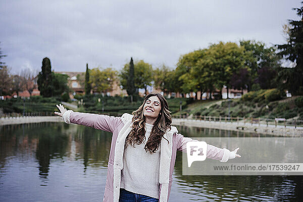 Smiling young woman with arms outstretched at lakeside