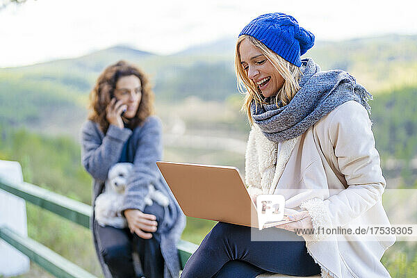Happy woman using laptop sitting on railing