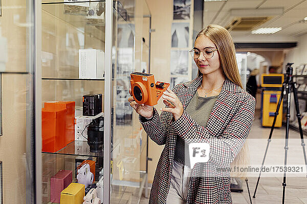 Young woman examining instant camera in shop