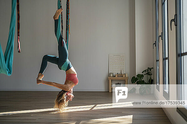 Woman hanging upside down on aerial silk practicing yoga at health club