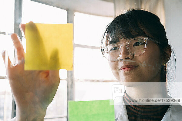 Young scientist sticking adhesive note on transparent glass in laboratory