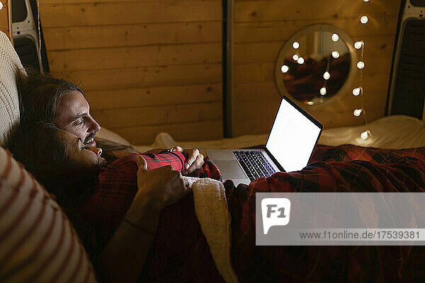 Couple using laptop lying on bed in camper van