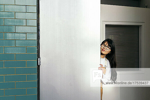 Young woman peeking from behind white door