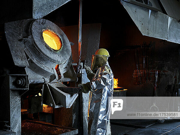 Blue-collar worker melting metal in furnace at industry