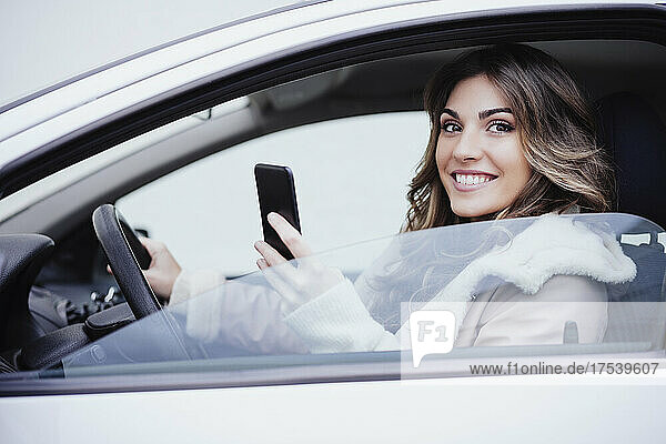 Smiling woman holding smart phone in car